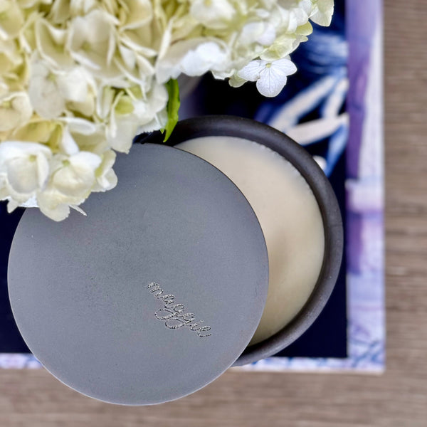 Custom concrete candle in charcoal gray. An example of the engraved lid shows the dog naemorial came, "Magge" in an elegant script font. Each concrete candle is 5.5" in diameter and 3.5" deep with three wicks to burn evenly. Choose a fragrance sucj as Rolling in the grass, Big Stick and also Unscented. Makes the perfect custom pet memorial gift.