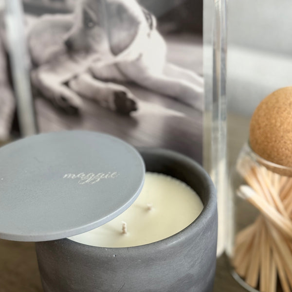 Custom concrete candle in charcoal gray. An example of the engraved lid shows the dog naemorial came, "Magge" in an elegant script font. Each concrete candle is 5.5" in diameter and 3.5" deep with three wicks to burn evenly. Choose a fragrance sucj as Rolling in the grass, Big Stick and also Unscented. Makes the perfect custom pet memorial gift.