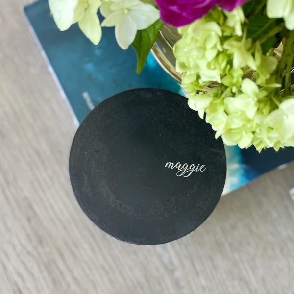 Custom concrete mndle in charcoal gray. An example of the engraved lid shows the dog naemorial came, "Magge" in an elegant script font. Each concrete candle is 5.5" in diameter and 3.5" deep with three wicks to burn evenly. Choose a fragrance sucj as Rolling in the grass, Big Stick and also Unscented.  Makes the perfect custom pet memorial gift.